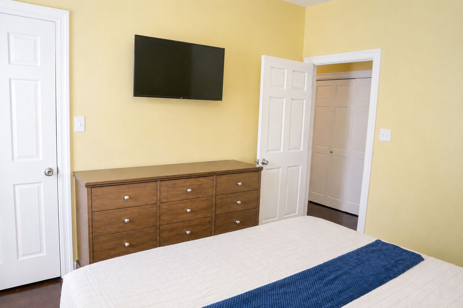 Une chambre à coucher avec un lit, une commode, un téléviseur et un placard.