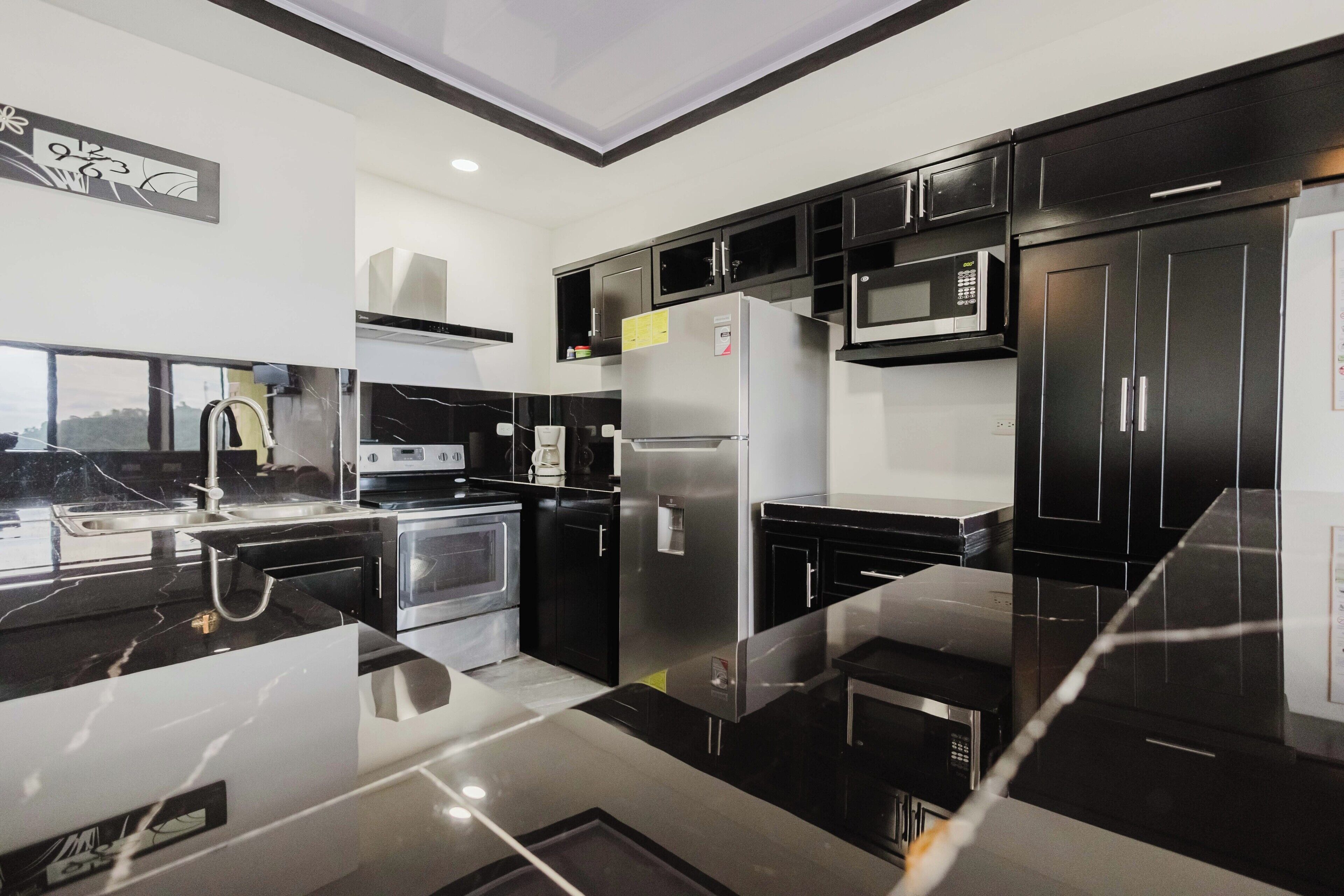 A modern kitchen with black cabinets, stainless steel appliances, and a marble countertop.