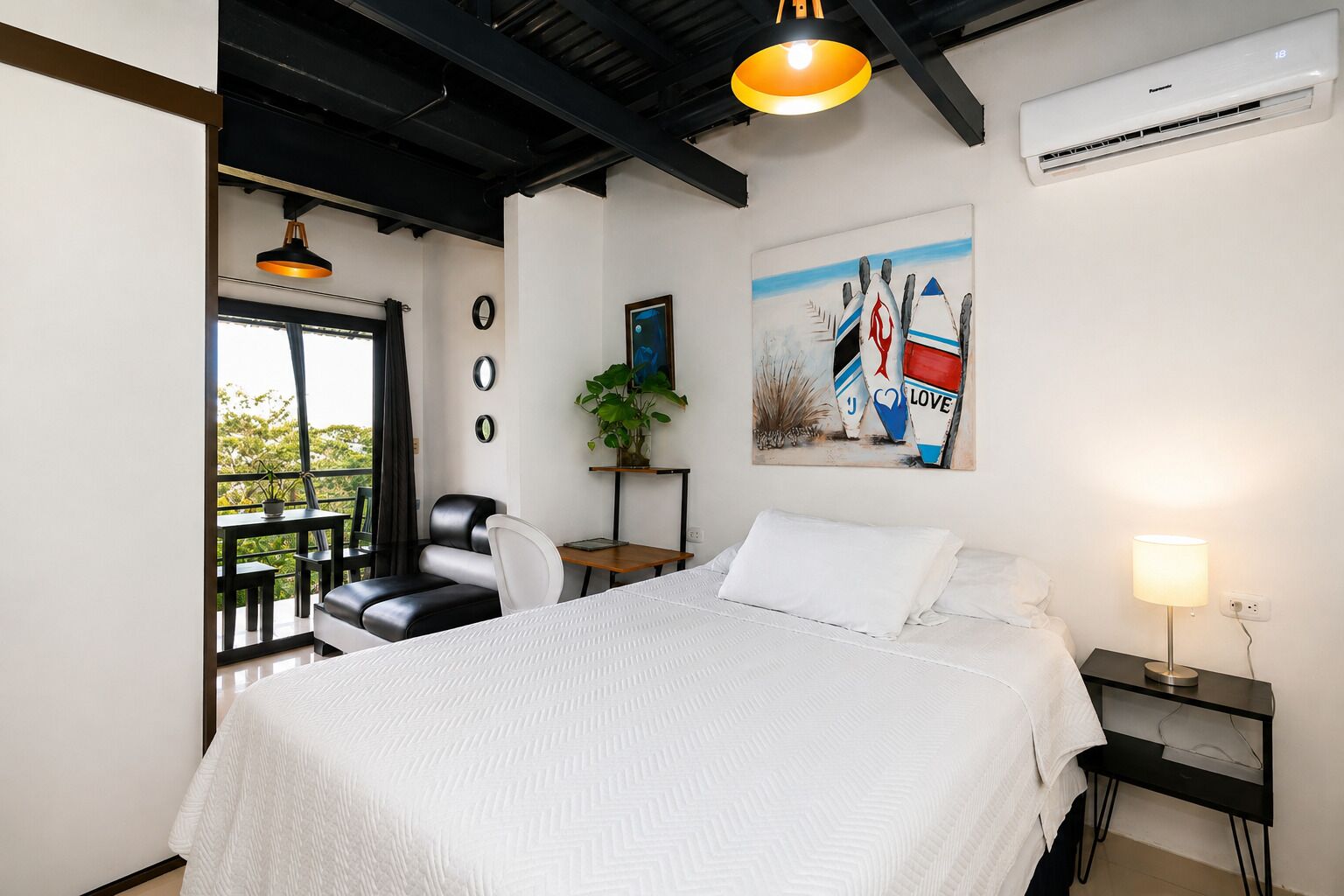 A bedroom with a bed, a desk, a chair, a potted plant, and a painting on the wall.