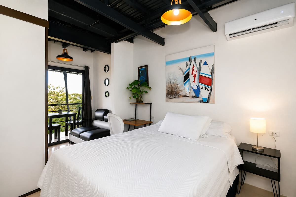 Ein Schlafzimmer mit Bett, Schreibtisch, Stuhl, einem Blumentopf und einem Bild an der Wand.
