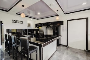Una cocina moderna con muebles negros y blancos, una isla central con taburetes y lámparas colgantes.