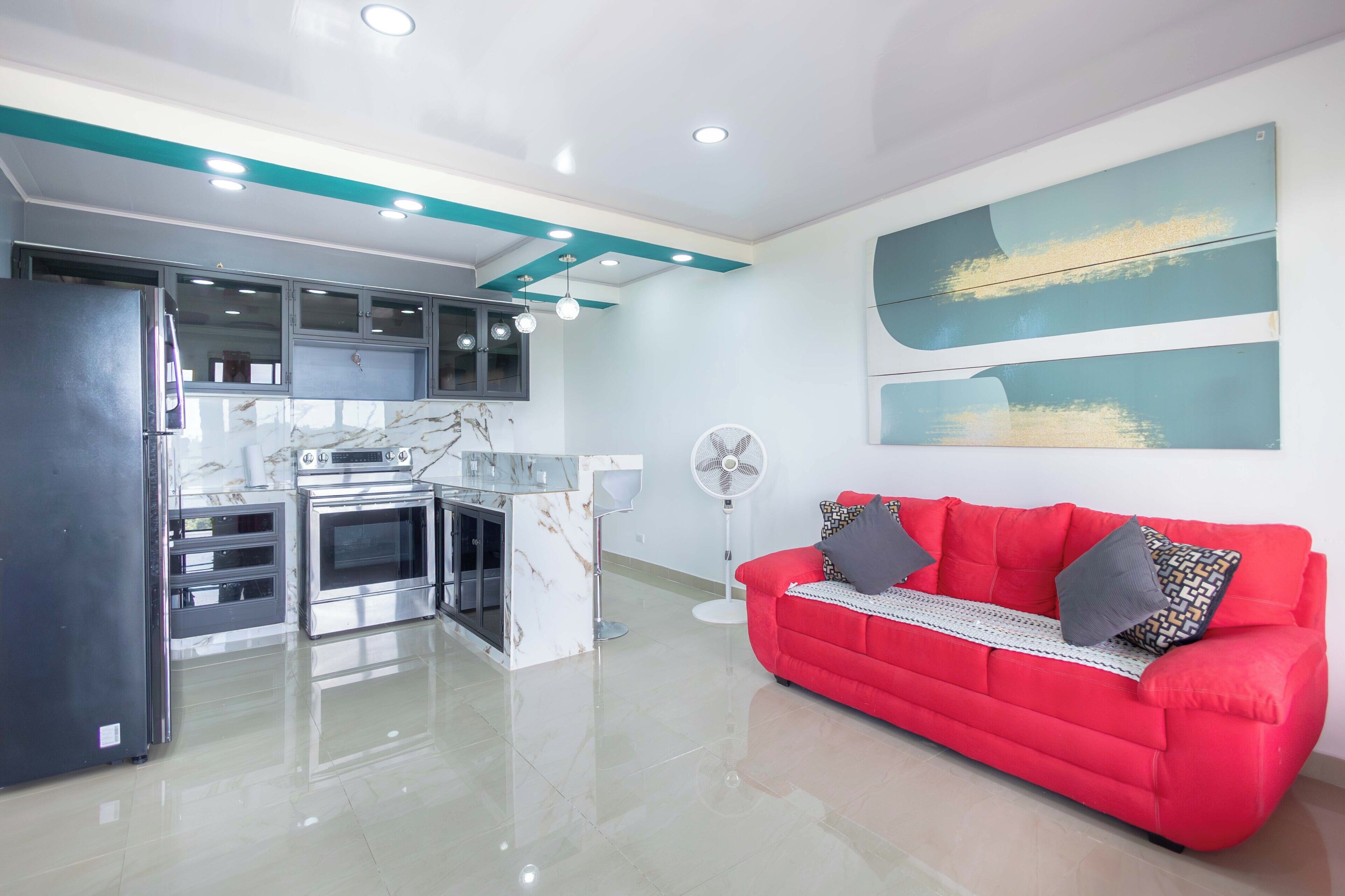 A modern kitchen with a marble countertop, stainless steel appliances, and a red sofa with patterned cushions.