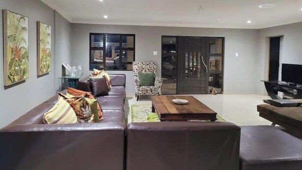 Een moderne woonkamer met een bank, een salontafel en een televisie. Twee schilderijen hangen aan de muur en er is een raam met uitzicht op het omliggende landschap.