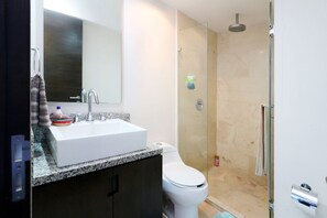Un baño moderno con lavamanos blanco, inodoro y ducha con mampara de vidrio.