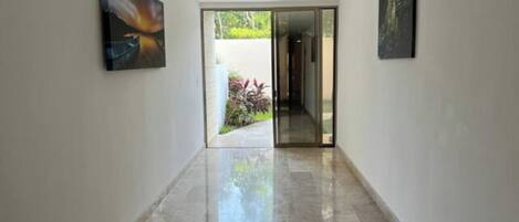 A hallway with a glass door leading to an outdoor area, flanked by two artworks on the walls.