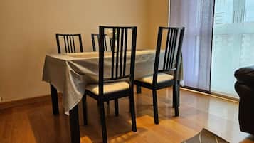 Un comedor con una mesa dispuesta para cuatro personas, sillas de madera, un tapete y una ventana con cortinas.
