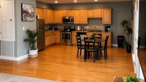 A modern kitchen with wooden cabinets, stainless steel appliances, and a dining area with a table and chairs. - Unwind After Work · 3BR 2BA · King Beds · W/D (Moss Point)