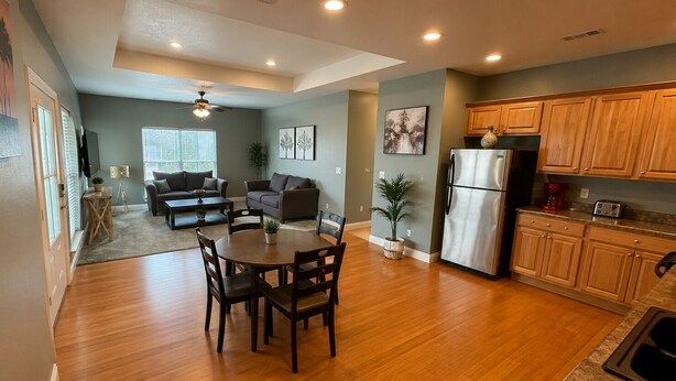A modern kitchen with wooden cabinets, a stainless steel refrigerator, and a dining area with a round table and chairs. - Unwind After Work · 3BR 2BA · King Beds · W/D (Moss Point)