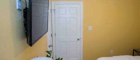 A room with a bed, a door, a wall-mounted TV, and a plant.