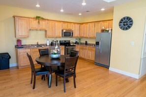 Una cocina con armarios de madera, microondas, estufa, refrigerador y una mesa de comedor con sillas.