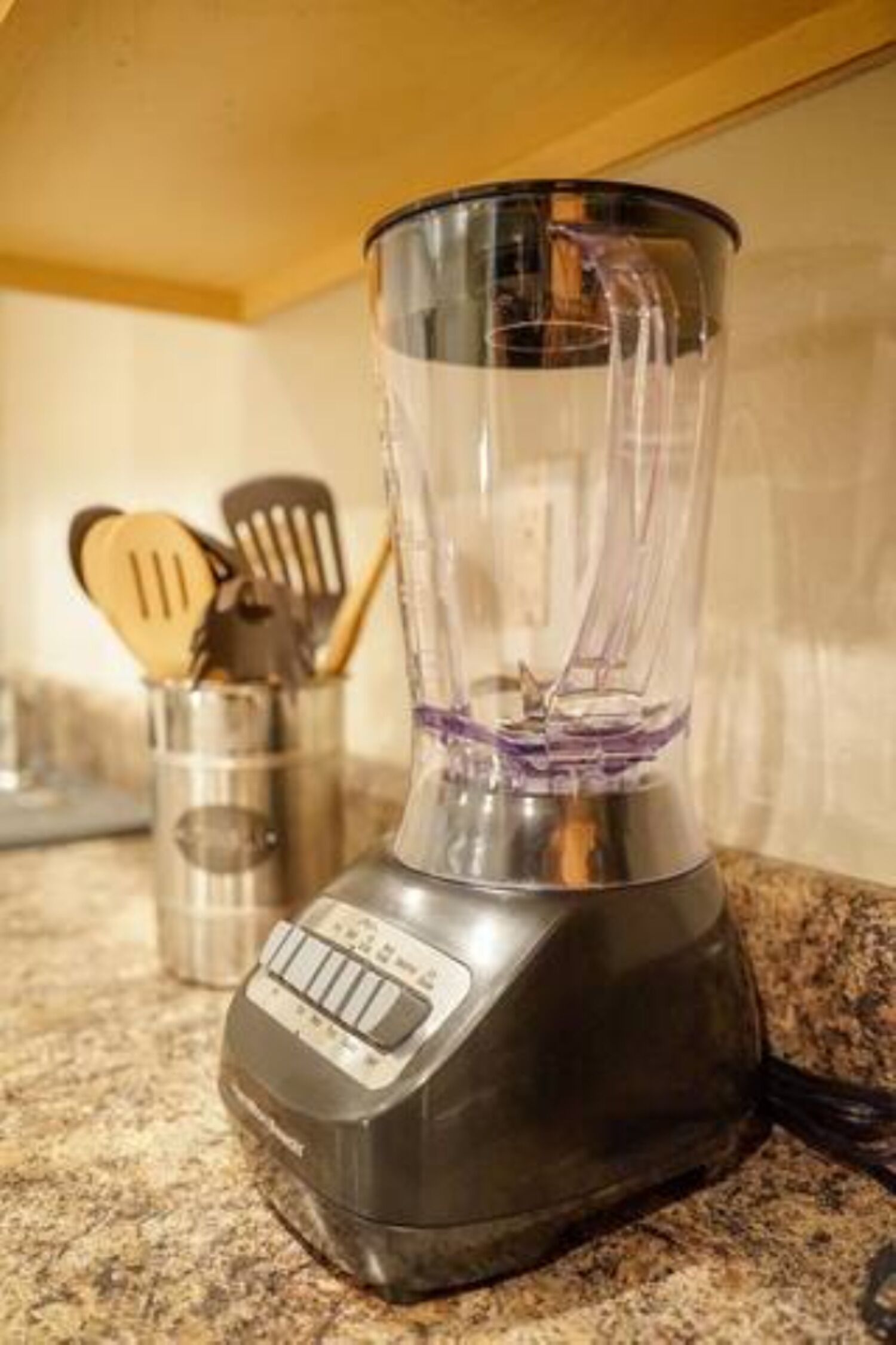 A kitchen with a blender on the counter, a metal utensil holder, and a wooden spatula.