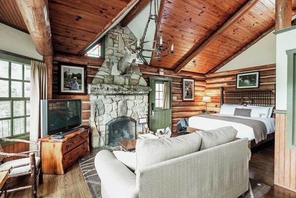 Cozy cabin-style room with a stone fireplace, comfortable sofa, and a neatly made bed.