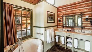 Une salle de bain de style chalet, avec une baignoire sur pieds, des murs en bois et un grand miroir au-dessus du lavabo.