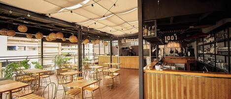 Un café amplio con mesas y sillas de madera, una zona de bar y ventanas grandes que dejan entrar luz natural.