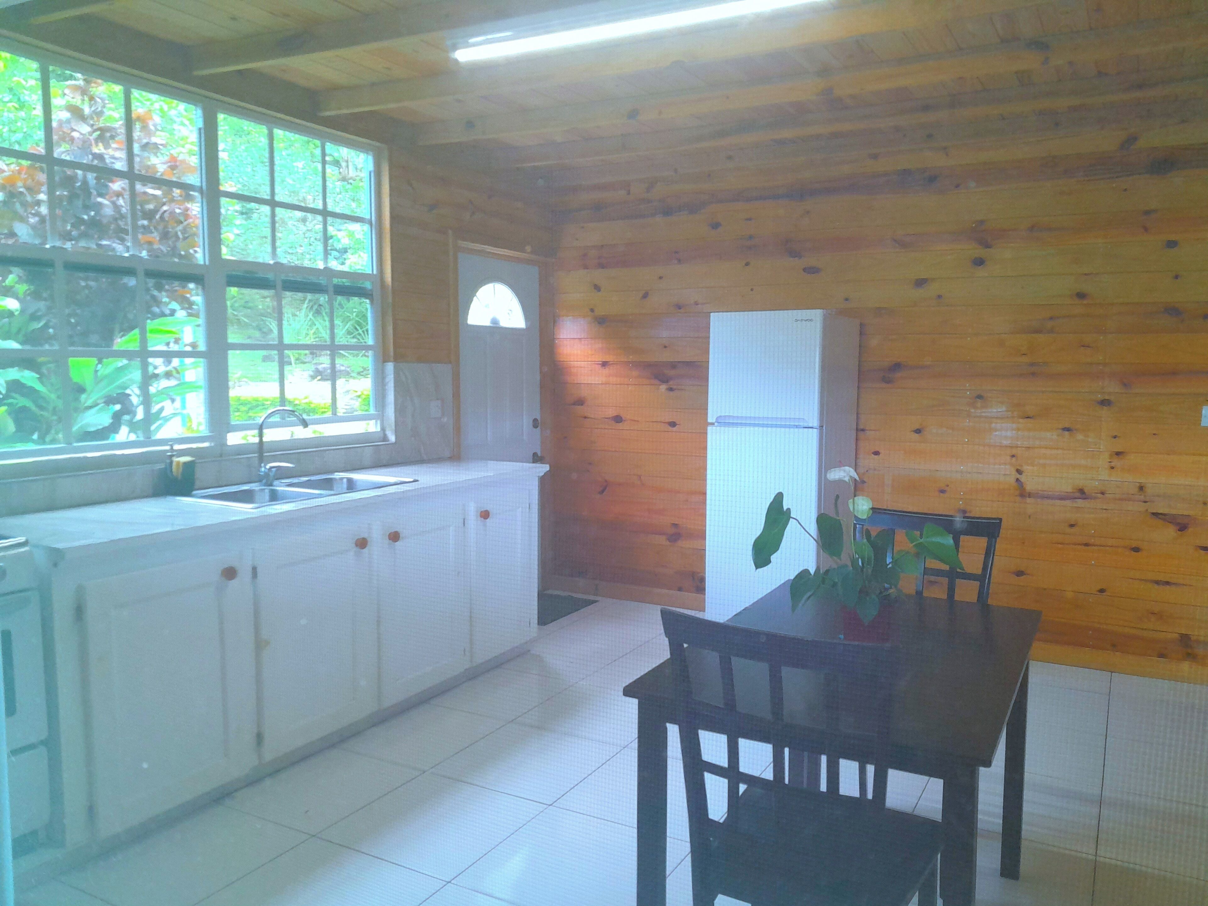 A kitchen with wooden walls, a white refrigerator, a sink, and a dining table with chairs.