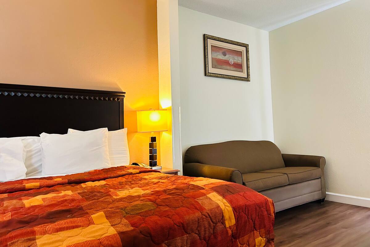 A hotel room with a bed, a couch, a lamp, and a framed picture on the wall.