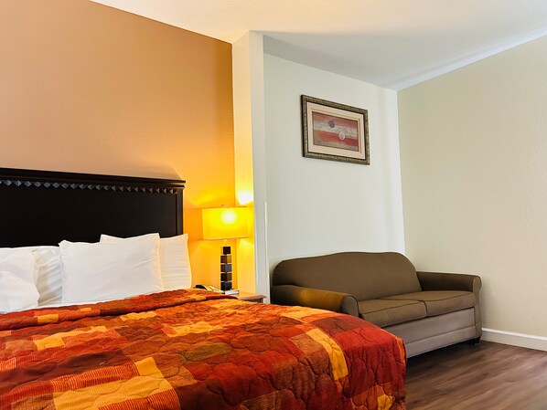 A hotel room with a bed, a couch, a lamp, and a framed picture on the wall. - The Best Inn & Suites (Markham)