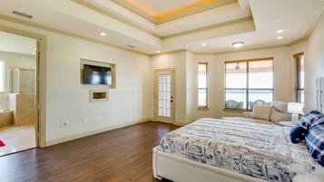 A spacious bedroom with a large bed, a television mounted on the wall, and a view of the outdoors through a window.