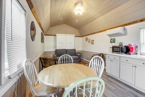 Une cuisine chaleureuse avec une table en bois, des chaises blanches, un canapé gris et un meuble blanc.