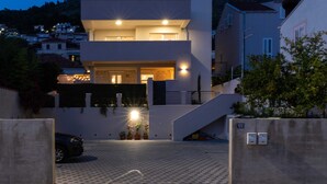 Un edificio moderno de dos pisos con techo plano, entrada visible y camino de entrada pavimentado que conduce a un acceso con puerta.