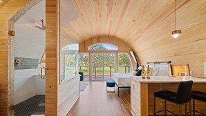 Un interior moderno de madera con un amplio ventanal arqueado, una pequeña zona de cocina y una ducha con puerta de vidrio.