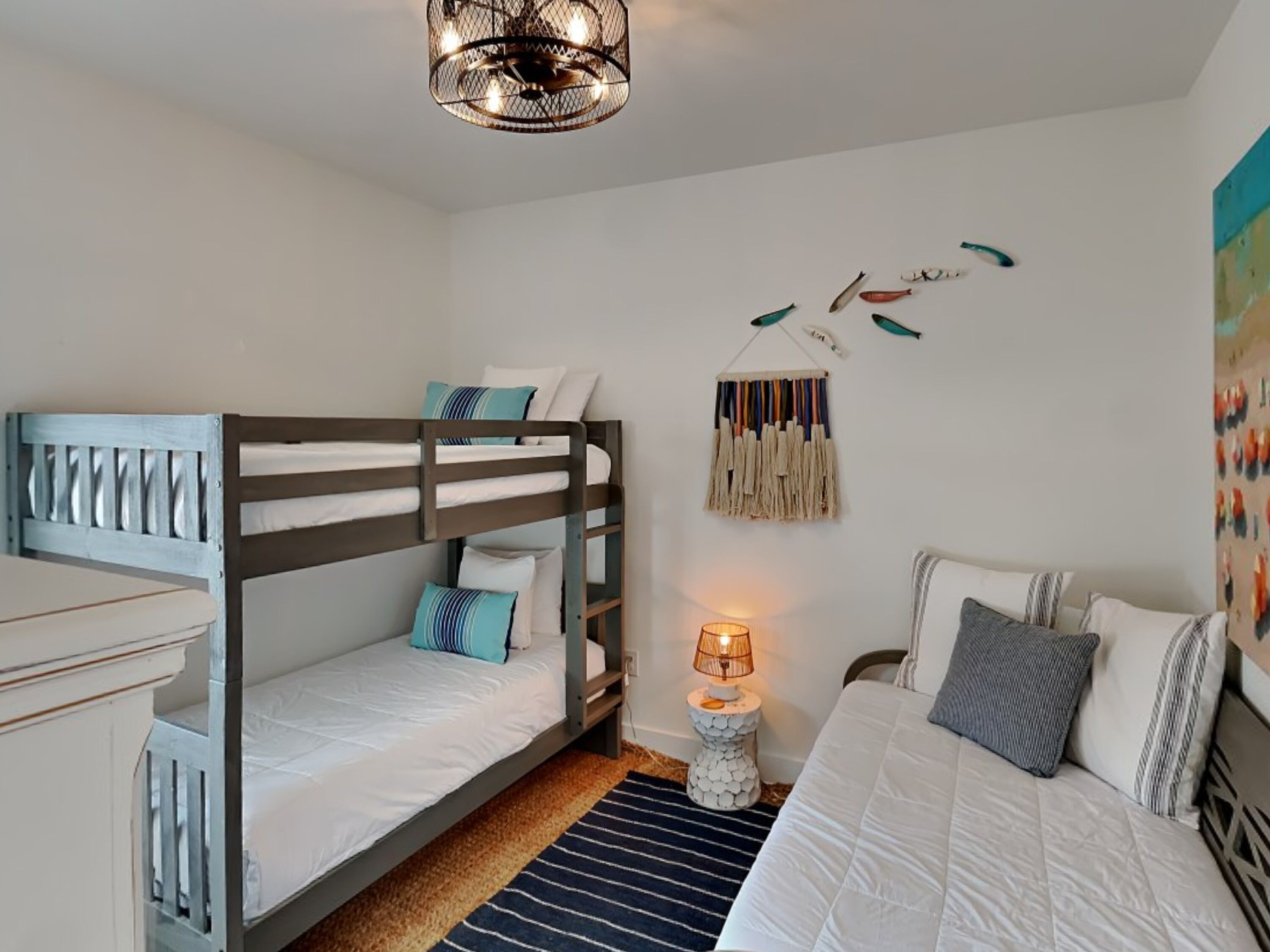 A bedroom with a bunk bed, a single bed, a lamp, and wall art.