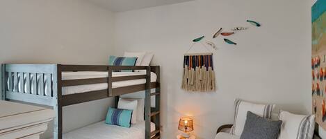 A bedroom with a bunk bed, a single bed, a lamp, and wall art.