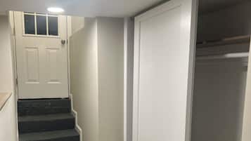 A narrow hallway with a wooden staircase leading to a white door.