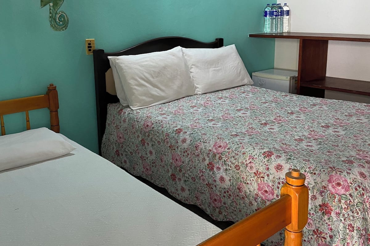 A room with two beds, a wooden headboard, a teal wall, a decorative seahorse, a shelf with water bottles, and a bedside table.