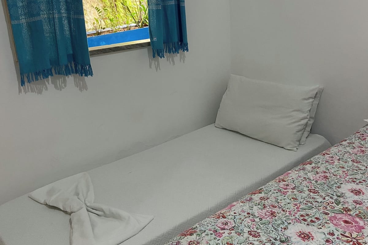 A single bed with a floral bedspread, a white pillow, and a blue curtain.