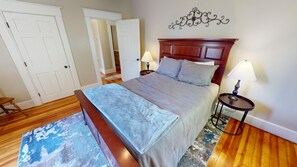 Une chambre à coucher avec un grand lit, deux tables de chevet, une tête de lit en bois, un tapis à motifs et une porte blanche.