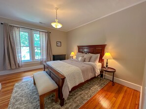 A bedroom with a wooden bed, two bedside lamps, a bench, a rug, and a window with curtains. - 1st Choice Lodging- Maple Leaf Inn (Nelsonville)
