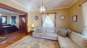 A living room with a beige sofa, a patterned rug, a wooden staircase, and a clock on the wall. - 1st Choice Lodging- Maple Leaf Inn (Nelsonville)