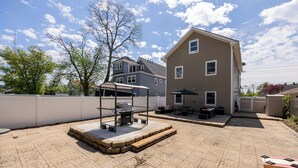 A backyard with a barbecue grill, outdoor seating, and a house.