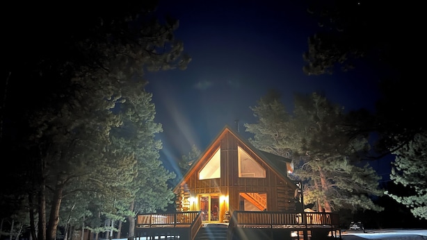 A log cabin with a wooden deck, large windows, and a staircase leading to the entrance.