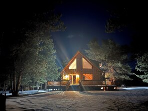 A log cabin with a wooden deck, large windows, and a staircase leading to the entrance.