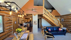 A cozy log cabin interior with a dining area, a sofa, and a staircase leading to an upper level.