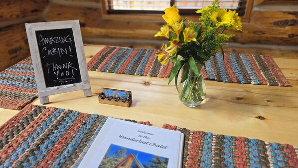 A wooden table with a blackboard sign, a vase with yellow flowers, a welcome sign, and woven placemats.