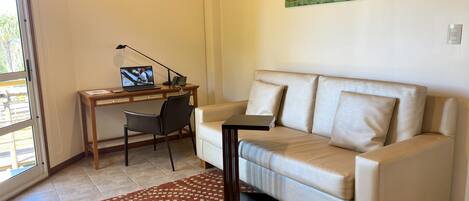 Un salon avec un canapé beige, un bureau avec un ordinateur portable, une chaise et un tapis à motifs.