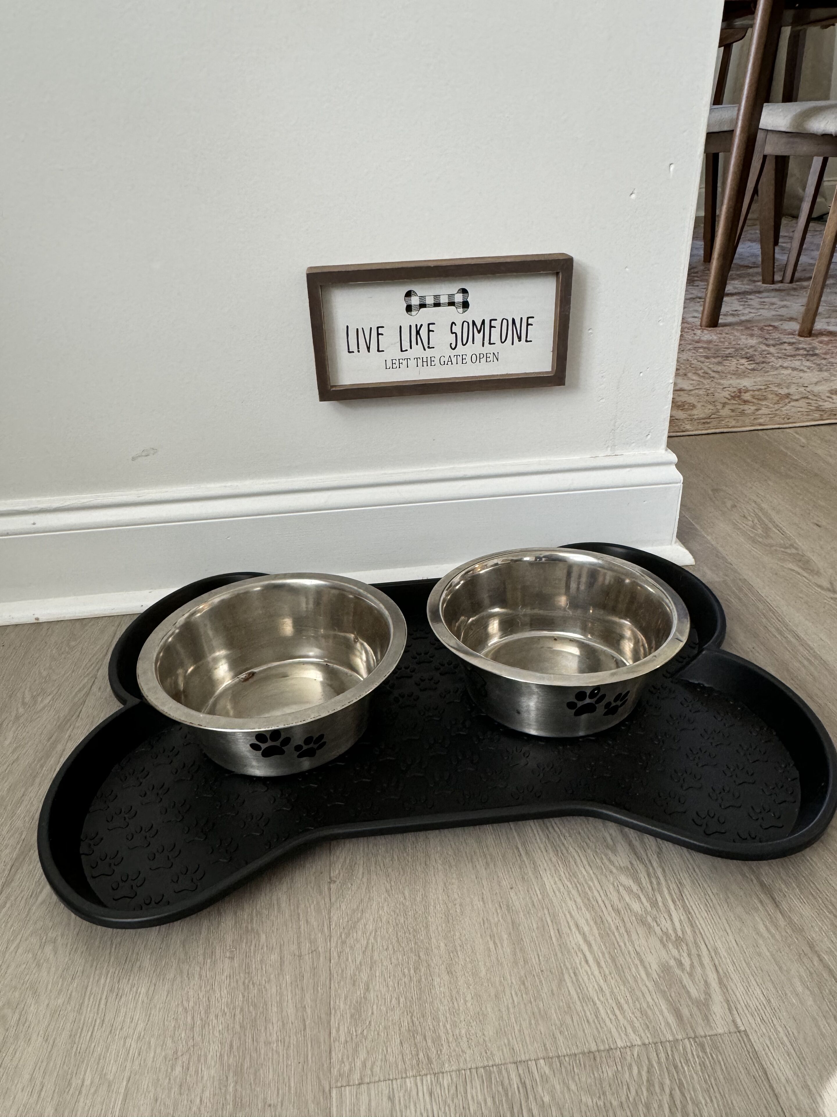 A pet feeding station with two stainless steel bowls on a black tray against a white wall.