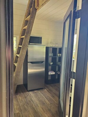 Compact kitchen with refrigerator, microwave, and glass-fronted cabinet.