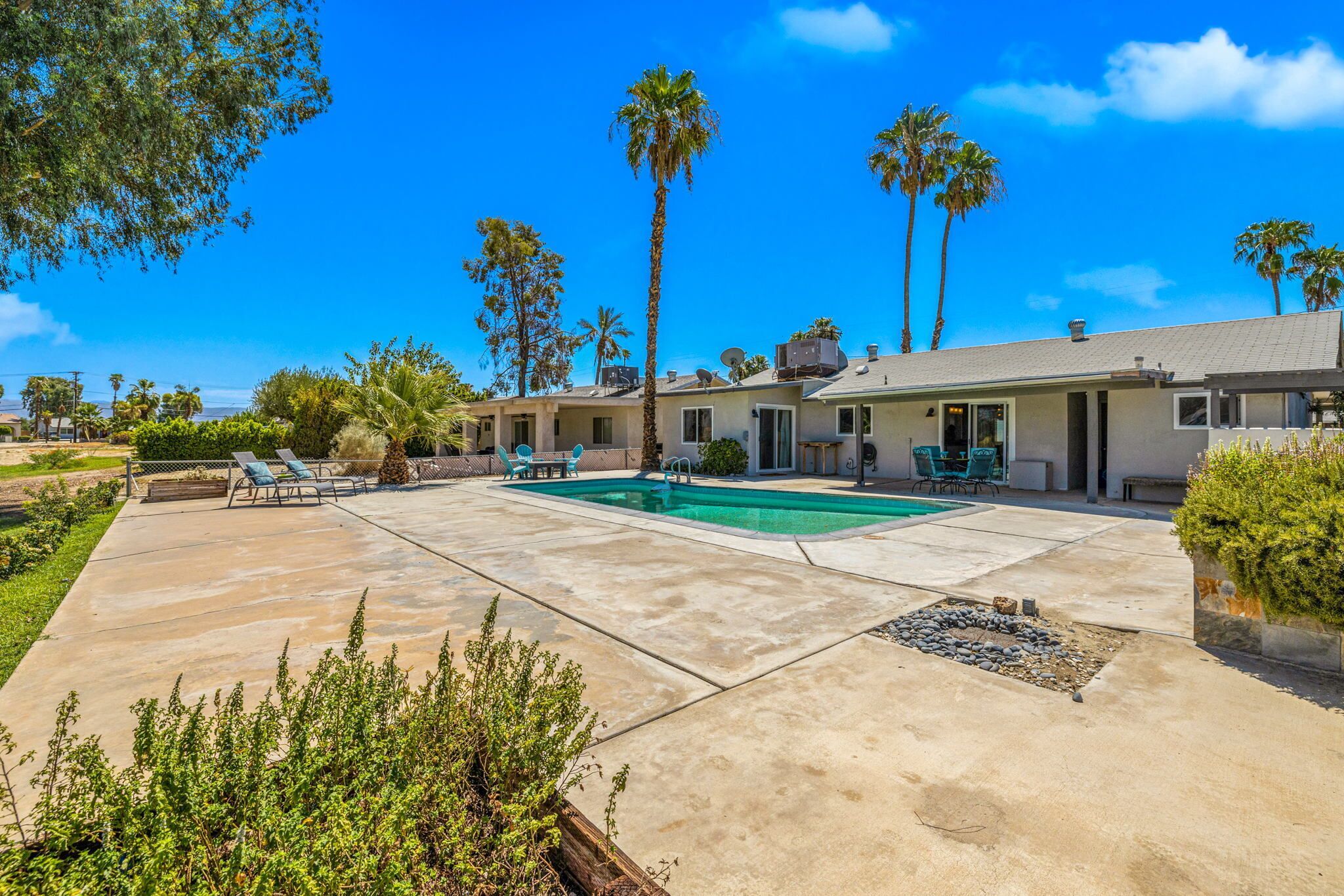 A residential property with a swimming pool, patio furniture, and palm trees.