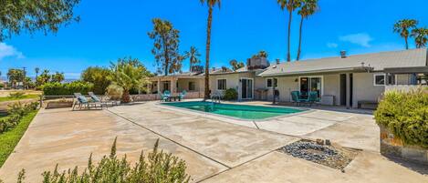 A residential property with a swimming pool, patio furniture, and palm trees.