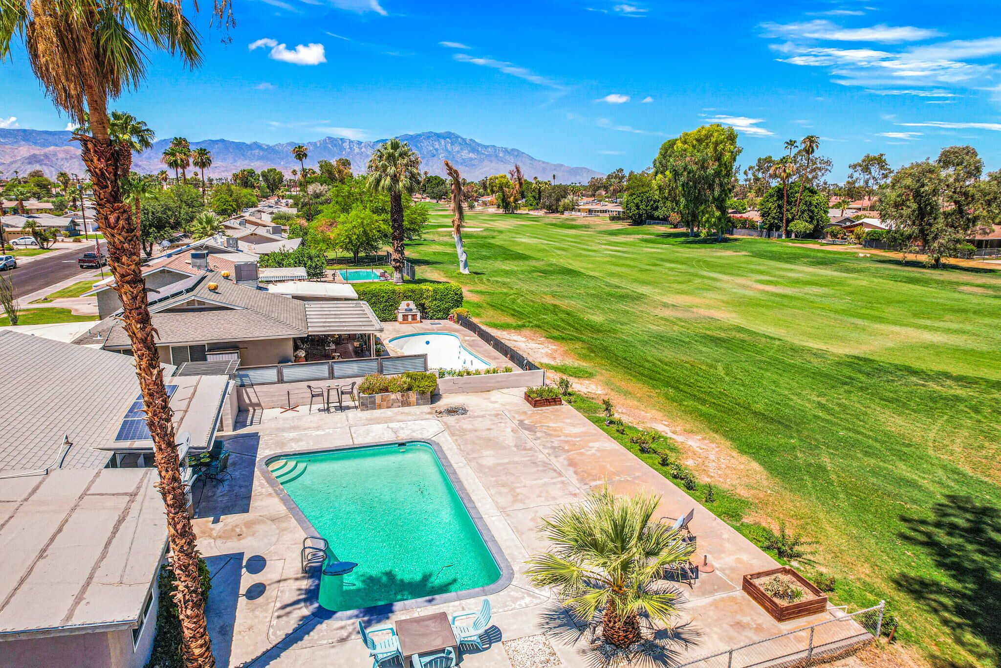 A residential area with a swimming pool, patio furniture, and a view of mountains.