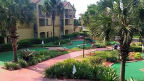 A golf course with a red pathway, green grass, palm trees, and a building in the background. - Orlando Christmas Week! (Orlando)