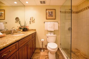 Baño con lavamanos de encimera de granito, armarios de madera, inodoro y ducha con mampara de vidrio.