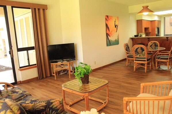 A living room with a sofa, a glass-top coffee table, a television, and a dining area with chairs and a table.