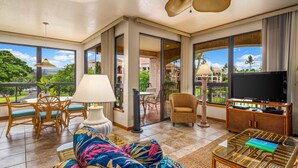 A spacious living room with a large window, a ceiling fan, a television, and a dining area.
