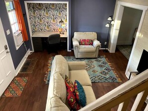Cozy living space with a sofa, armchair, and area rug, featuring a desk and staircase.