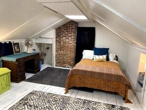 Cozy attic-style bedroom with a single bed, bedside table, and desk, set against a rustic brick wall.